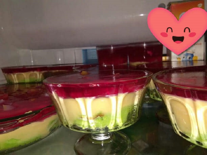 Puding trifle berlapis dengan swiss roll, kastard, buah koktel dan jelly dalam mangkuk jernih.