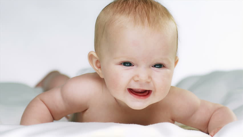 Gambar bayi berumur 4 bulan sedang berbaring tersenyum memandang ke kamera.