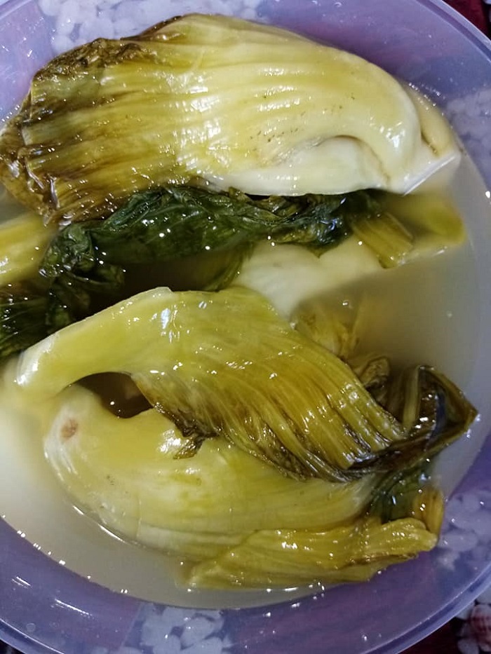 Sebuah mangkuk berisi sawi jeruk atau kai choy yang dimasak bersama ikan patin dan kuahnya berwarna kuning.