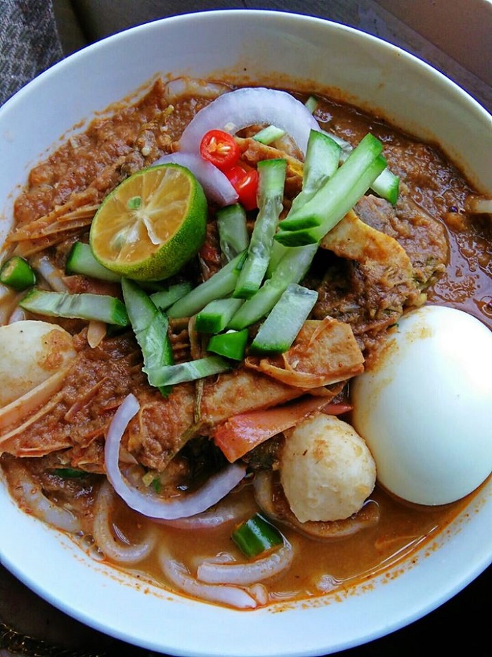 Sebuah mangkuk berisi laksa AEON dengan kuah asam pedas dan hiasan.