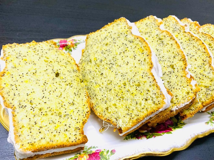 Sepotong kek poppy lemon dengan lapisan gula aising di atas kek berbentuk loaf.