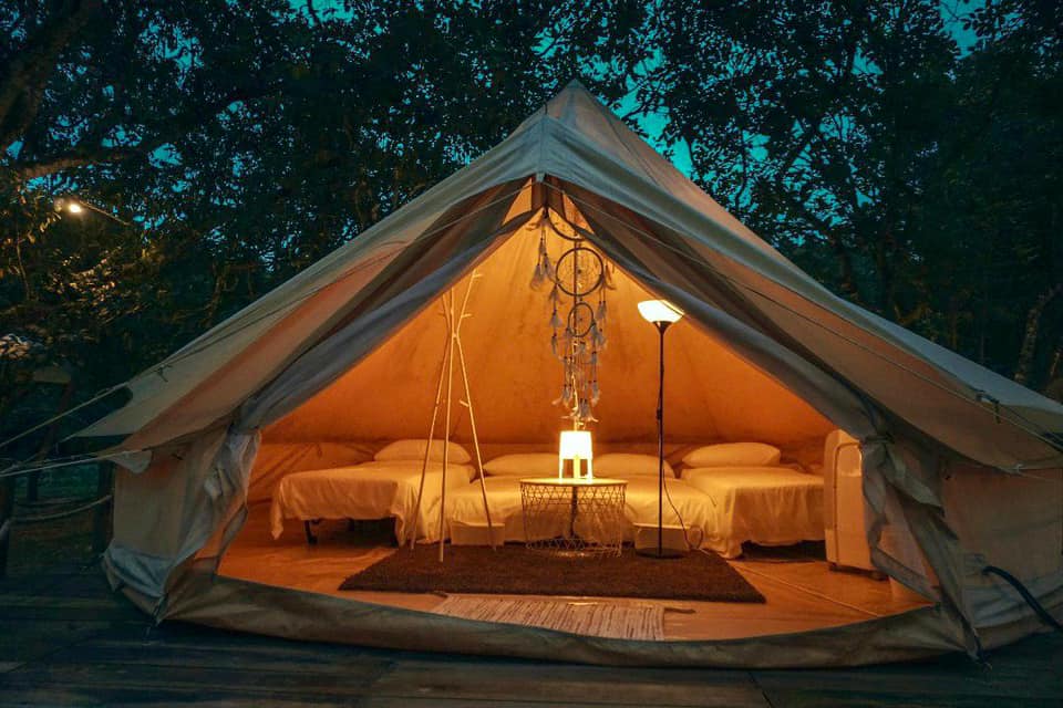 Pemandangan khemah glamping estetik di kawasan berhampiran sungai dikelilingi kehijauan alam sekitar.