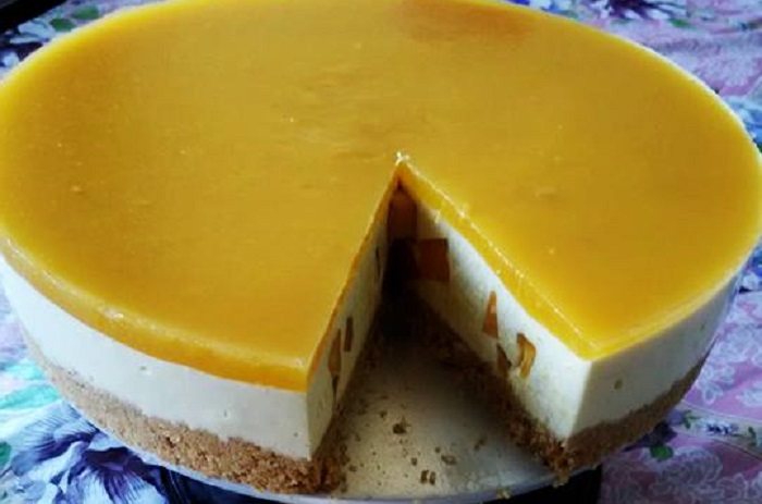Kek mango cheesecake dengan topping puree mangga berwarna kuning cerah diletakkan di atas loyang springform.