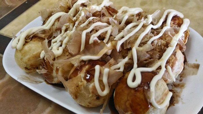 Gambar kuih takoyaki berbentuk bulat dengan topping mayonis dan serbuk bonito.