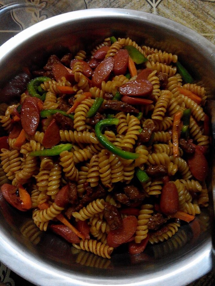Gambar hidangan spaghetti goreng spiral bersama daging cincang, sosej, dan sayur-sayuran dalam pinggan.