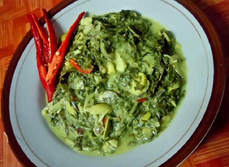 Sambal tempoyak daun kayu masak lemak berwarna gelap di dalam mangkuk