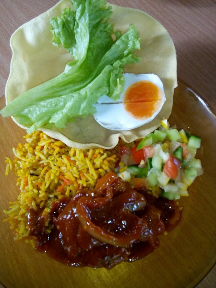 Hidangan nasi beriani gam berwarna kuning dengan ayam dan daun pudina dalam pinggan.