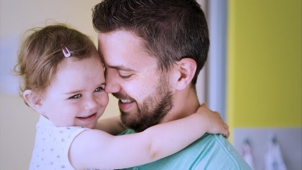 Bayi tersenyum dan gembira berada dalam pelukan ibu bapanya.