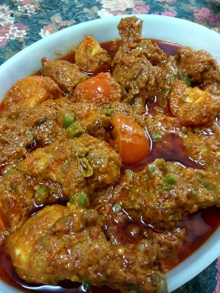 Sebekas ayam masak tomato berkuah merah pekat berserta hiasan cili dan daun.