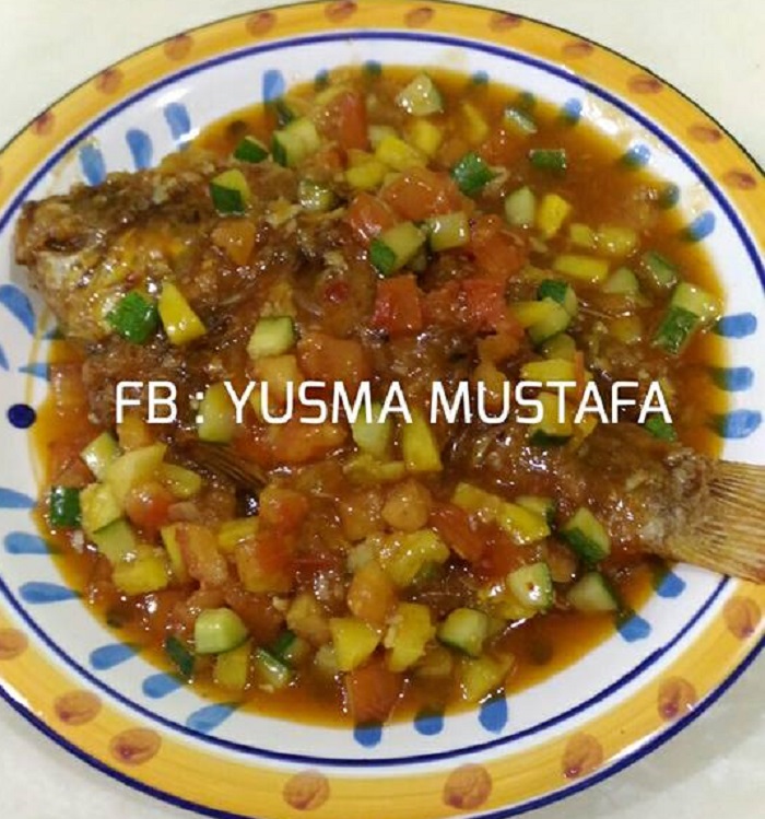 Se ekor ikan goreng masak tiga rasa dengan sos merah, hirisan nenas, tomato dan timun di atas pinggan.