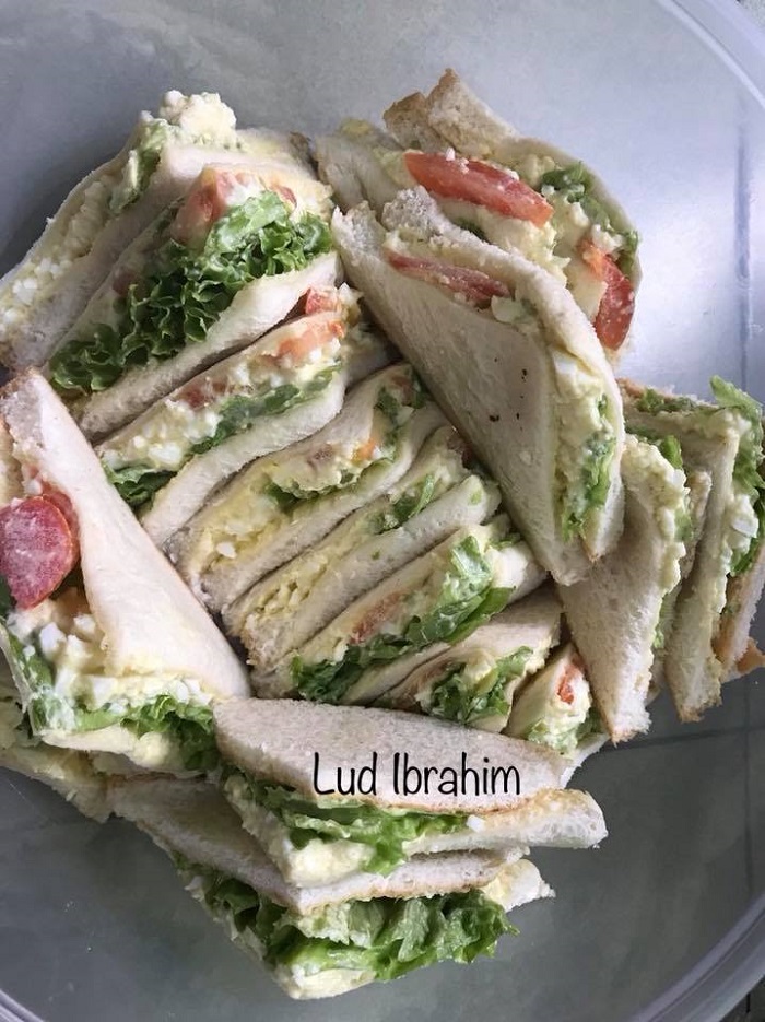 Roti sandwich telur yang dipotong segitiga bersama ulaman salad dan tomato.