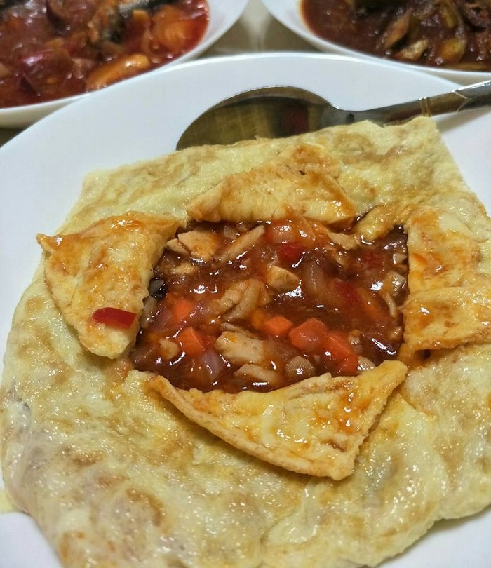 Gambar hidangan telur bungkus ala Thai yang dipotong menampakkan isi ayam dan sayur-sayuran di dalamnya
