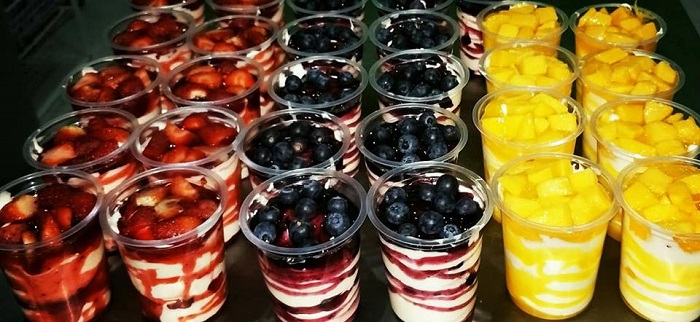 Mangkuk berisi aiskrim yogurt homemade creamy dengan topping buah-buahan segar dan sos blueberry.