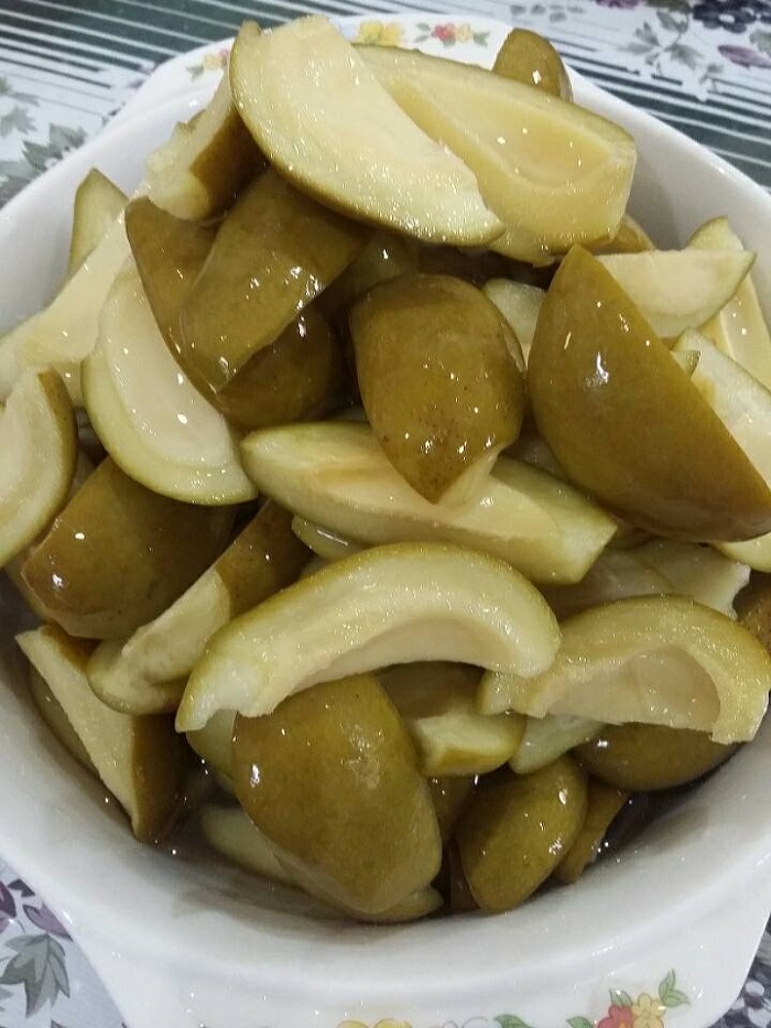 Sebekas jeruk mangga muda yang dipotong kecil dalam air gula berwarna kuning keemasan.