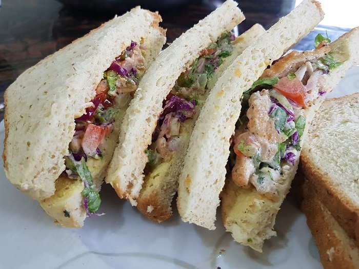 Gambar sandwich ayam di atas pinggan dengan roti, isi ayam dan sayuran segar.