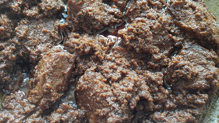 Hidangan rendang tok berwarna coklat gelap dengan potongan daging dan kelapa sangai dalam pinggan.