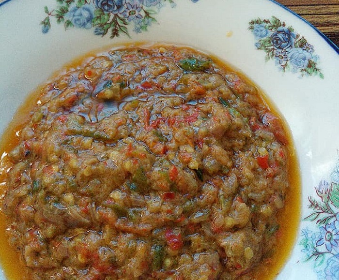 Sambal ayam penyet pedas berwarna merah dalam pinggan bersama nasi dan ayam.