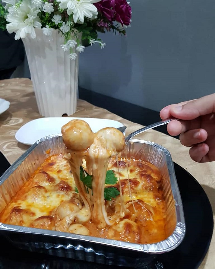 Bekas aluminium foil berisi meatball bolognese disalut cheese mozzarella yang telah dibakar.