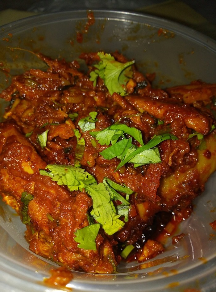 Hidangan ayam varuval masak garing ala India berwarna perang keemasan dengan rempah dan daun kari.