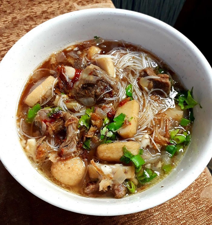 Sebuah mangkuk mee hoon sup dengan kuah penuh, dihias dengan daun sup dan bawang goreng