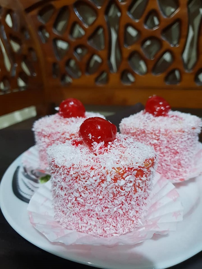 Kek madeline berbentuk loceng di atas pinggan, dihiasi ceri merah dan hijau.
