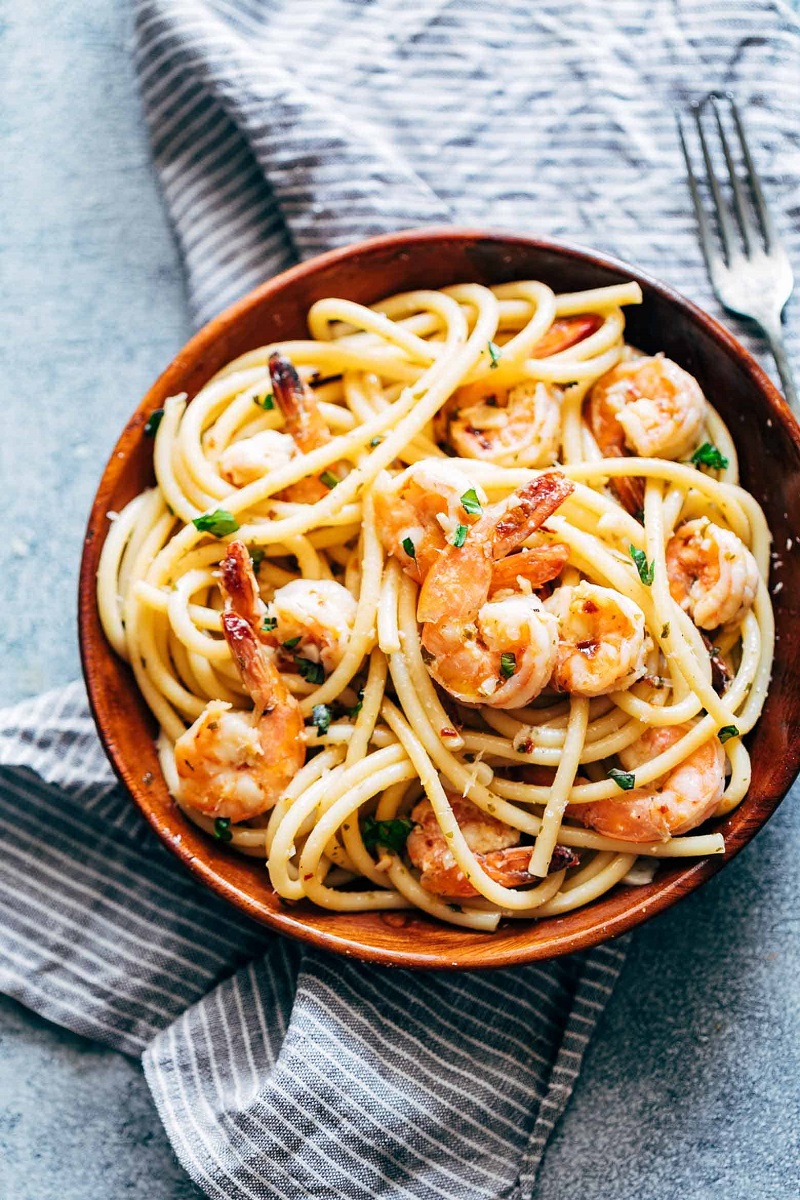 Penyajian spaghetti aglio olio dengan udang, tomato ceri, dan parsley di atas pinggan