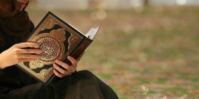 Ibu mengandung sedang membaca Al-Quran dengan senyuman.