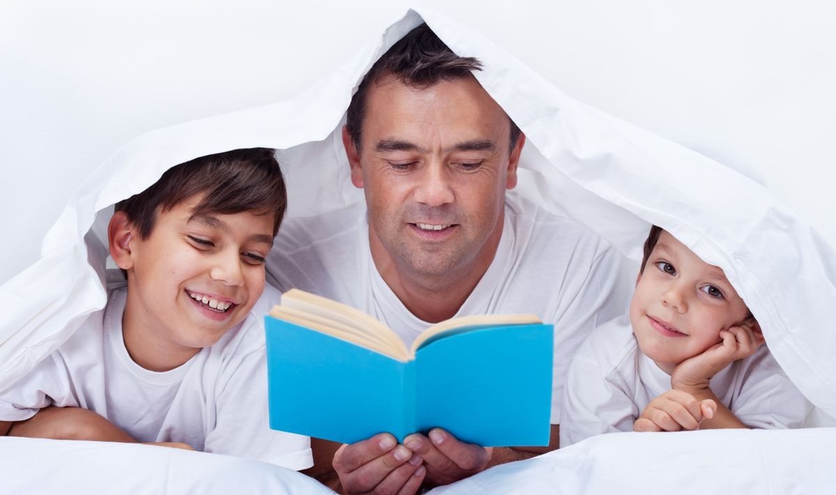 Seorang bapa membaca buku bersama anaknya di rumah.