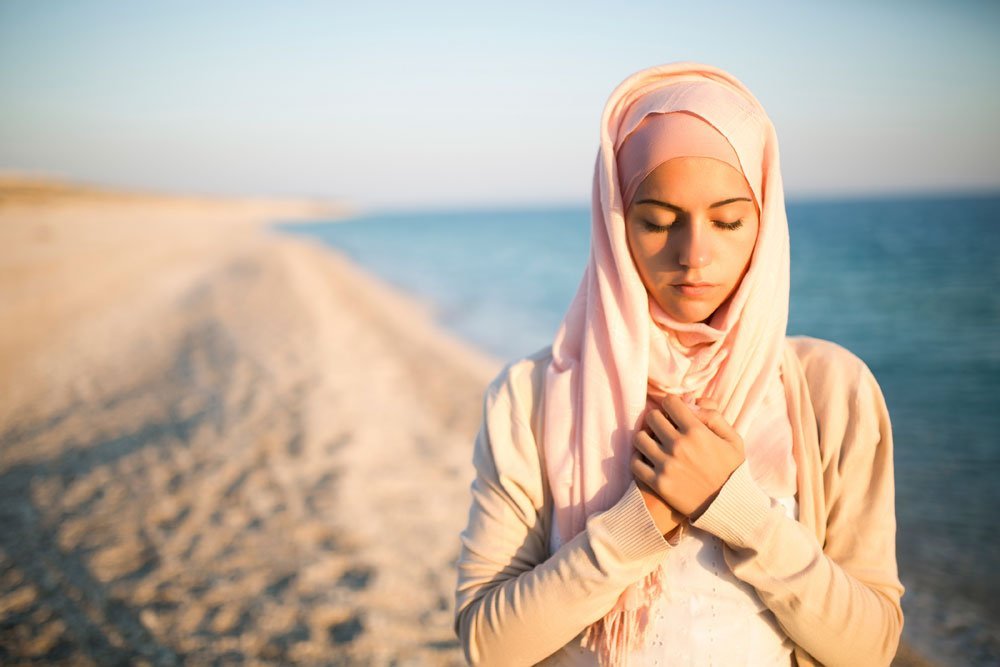 Wanita bertudung sedang duduk merenung ke luar tingkap dengan wajah tenang berfikir.