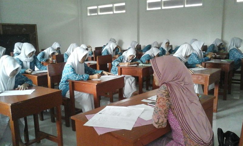 Guru Muslimah sedang mengajar di dalam kelas sebagai contoh adab murid terhadap guru.