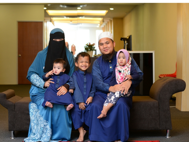 Suami dan isteri bergurau senda bersama anak-anak di ruang tamu sebagai gambaran keluarga sunnah.