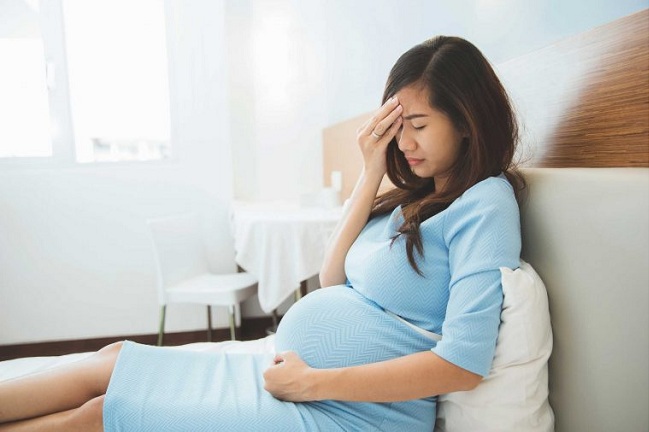 Wanita hamil duduk menyentuh perut berasa sakit atau tidak selesa sebagai gejala pra-eklampsia.