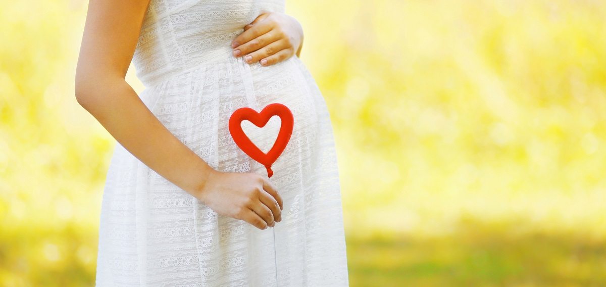 Ibu hamil memegang patung hati di atas perut sebagai simbol kasih sayang kepada bayi dalam kandungan.