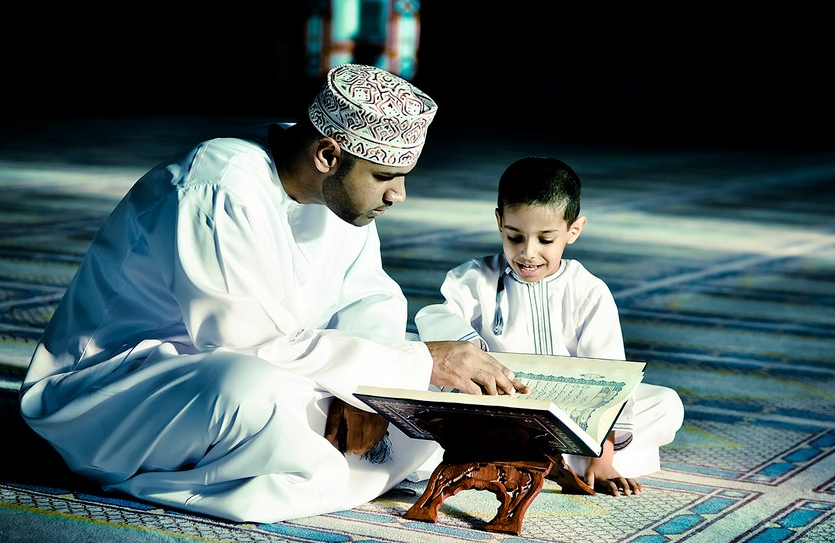 Ibu mengajar anak kecil membaca Al-Quran menggunakan papan rehal di dalam rumah.