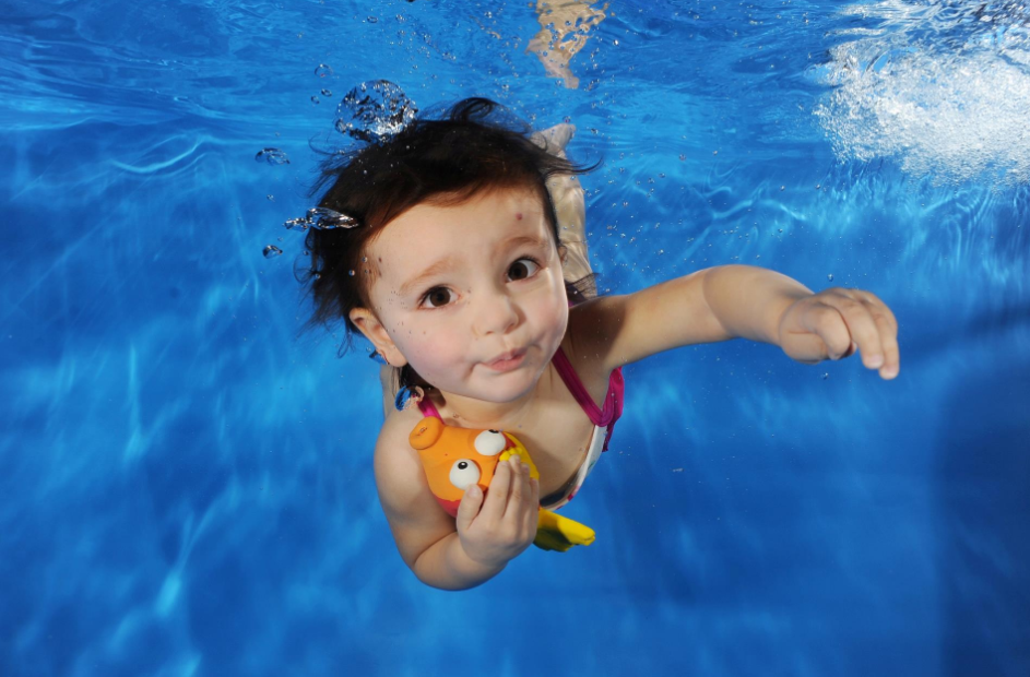Ibu bapa mengajar anak kecil berenang di dalam kolam renang sambil memakai pelampung.