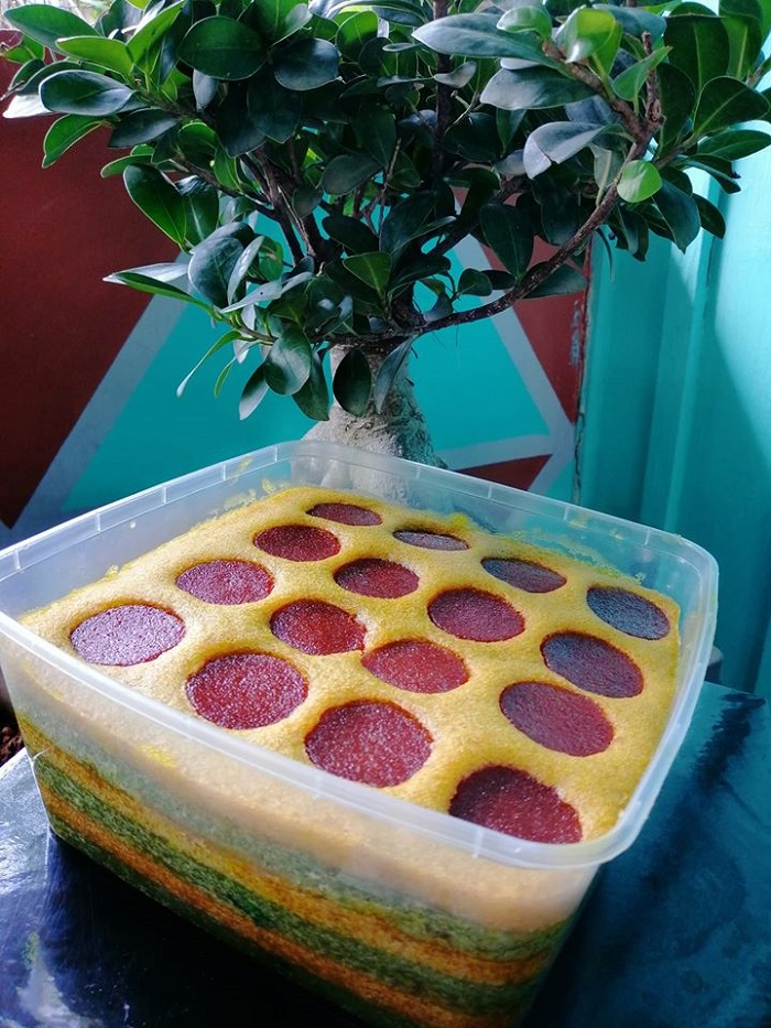 Kek lapis masam manis berlapis warna hijau dan kuning dengan hiasan asam manis di atasnya.