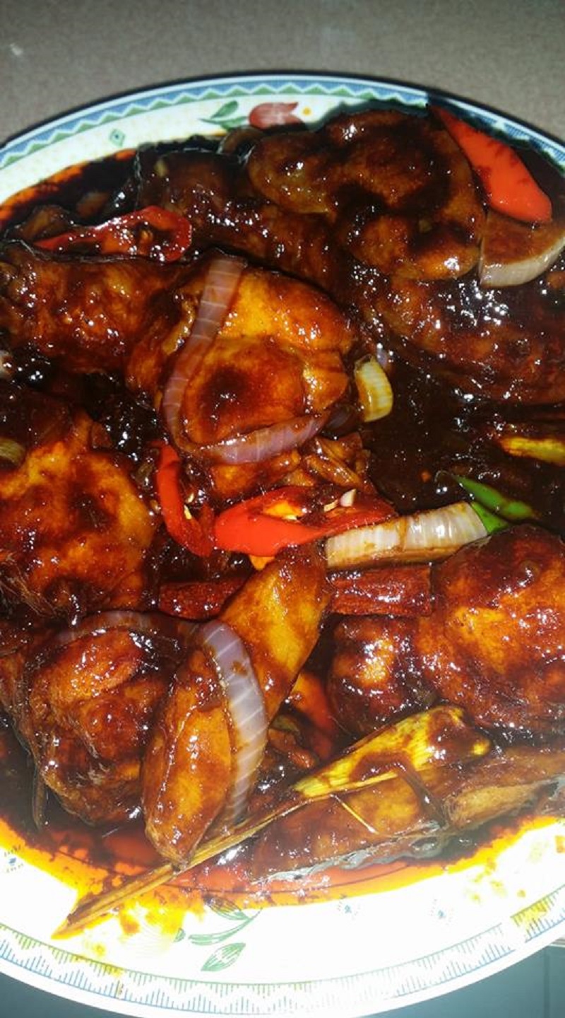 Hidangan ayam masak kicap keperangan berhiaskan daun kari dan cili padi di atas pinggan.