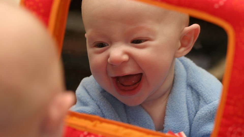 Bayi melihat diri sendiri pada cermin kecil