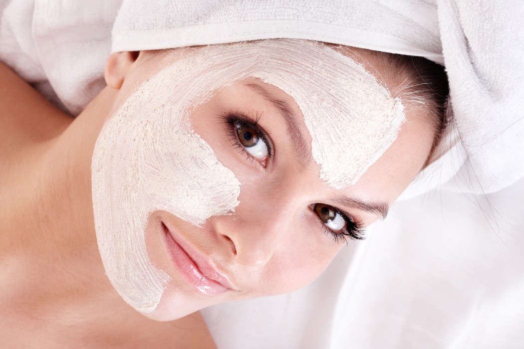 Wanita muda sedang membuat rawatan muka menggunakan topeng tanah liat (clay facial mask) di wajah.