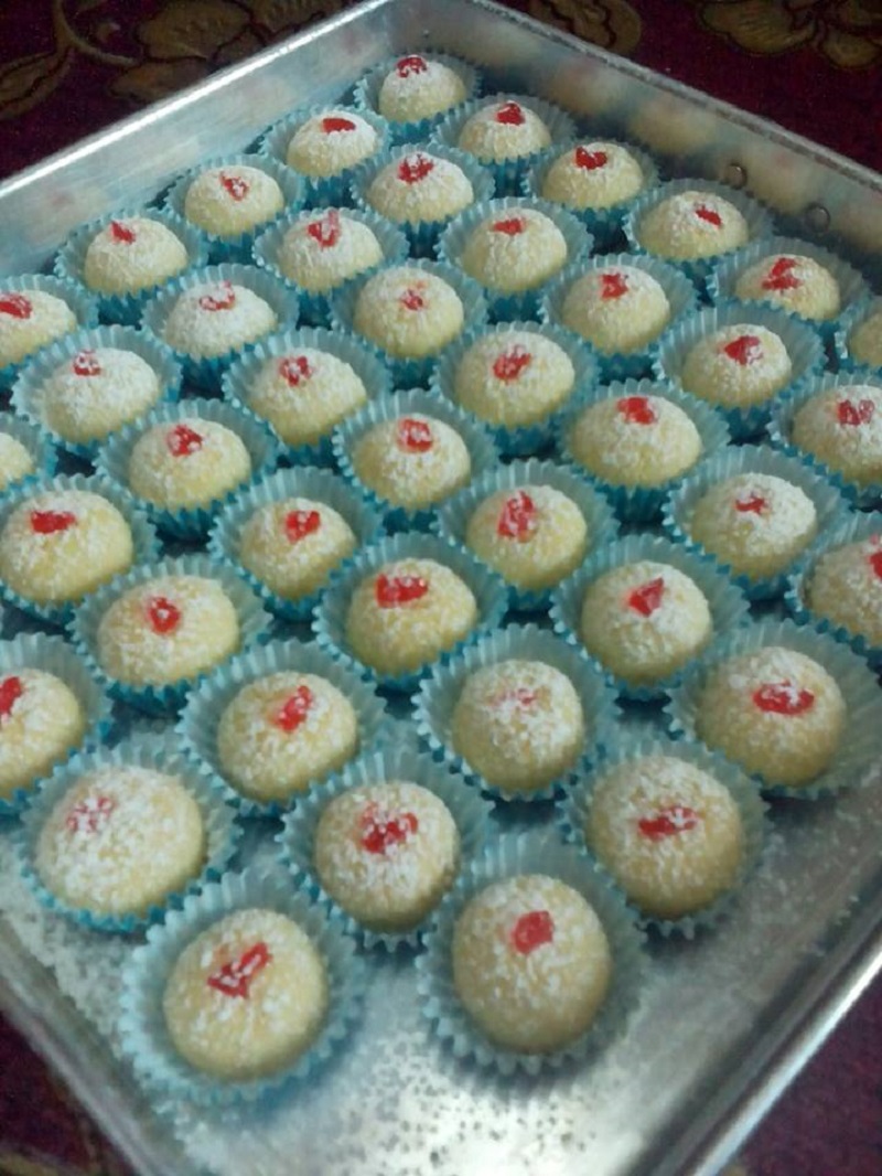 Biskut suji berbentuk bulat berwarna kekuningan tabur gula icing di atas paper cup