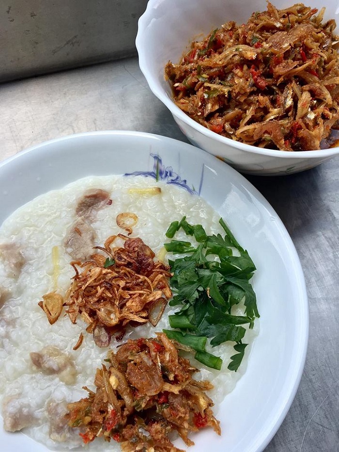 Sepinggan mangkuk bubur nasi panas dengan taburan ikan bilis goreng dan daun bawang.