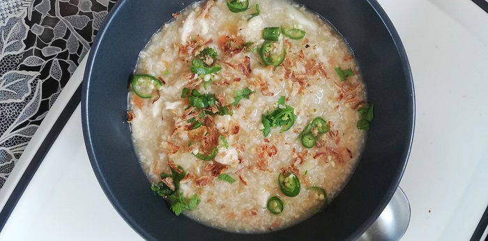 Sebuah mangkuk berisi bubur oat ayam yang sihat dengan hiasan daun sup dan bawang goreng.