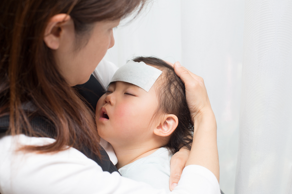 Gambarkan ibu menyentuh dahi anak yang sedang demam untuk memantau suhu badannya.
