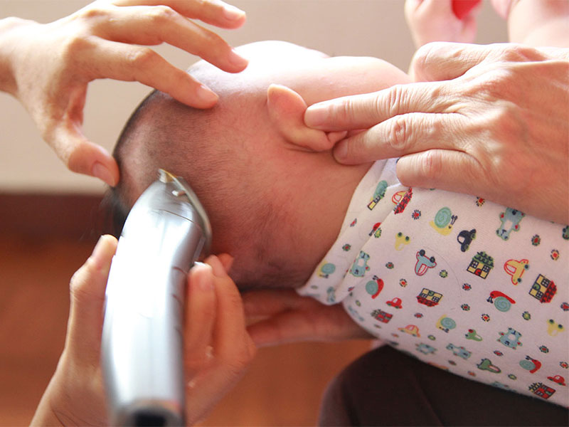 Bayi baru lahir sedang dicukur rambutnya dengan pisau pencukur secara berhati-hati.