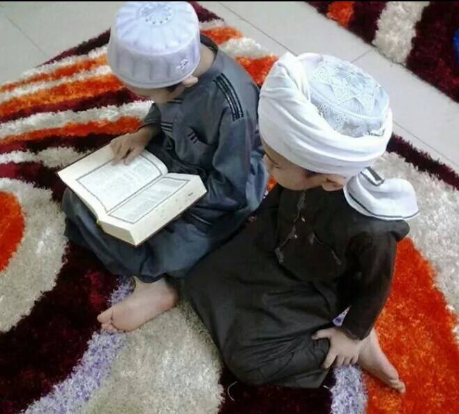 Kanak-kanak lelaki memakai jubah dan serban sedang memegang kitab Quran.