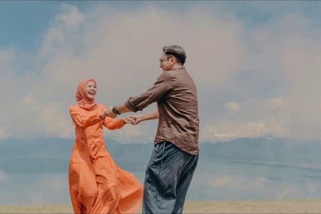 Gambar pasangan suami isteri sedang duduk berbicara mesra sambil tersenyum bahagia.