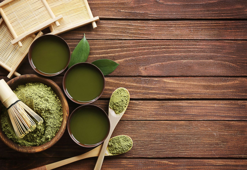 Secangkir teh hijau panas dengan daun teh di sebelahnya