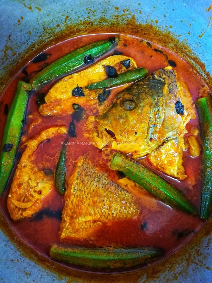 Sebuah pinggan berisi kari ikan merah dengan kuah pekat, bendi dan tomato.