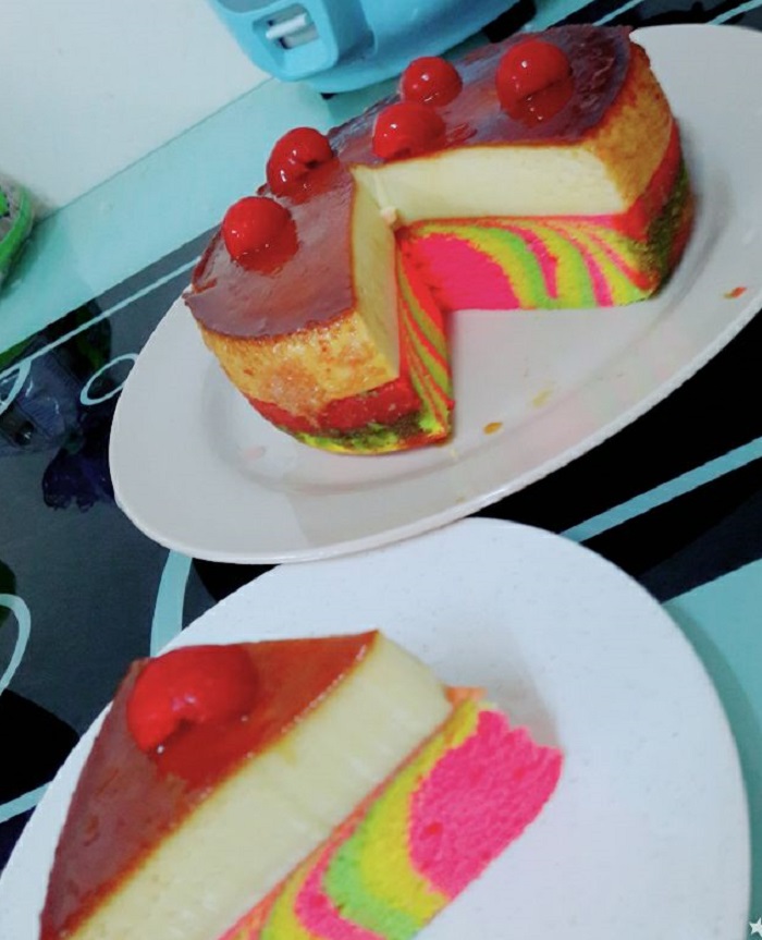 Sepotong kek pelangi karamel dengan lapisan puding dan apam berwarna-warni yang dihiris cantik.