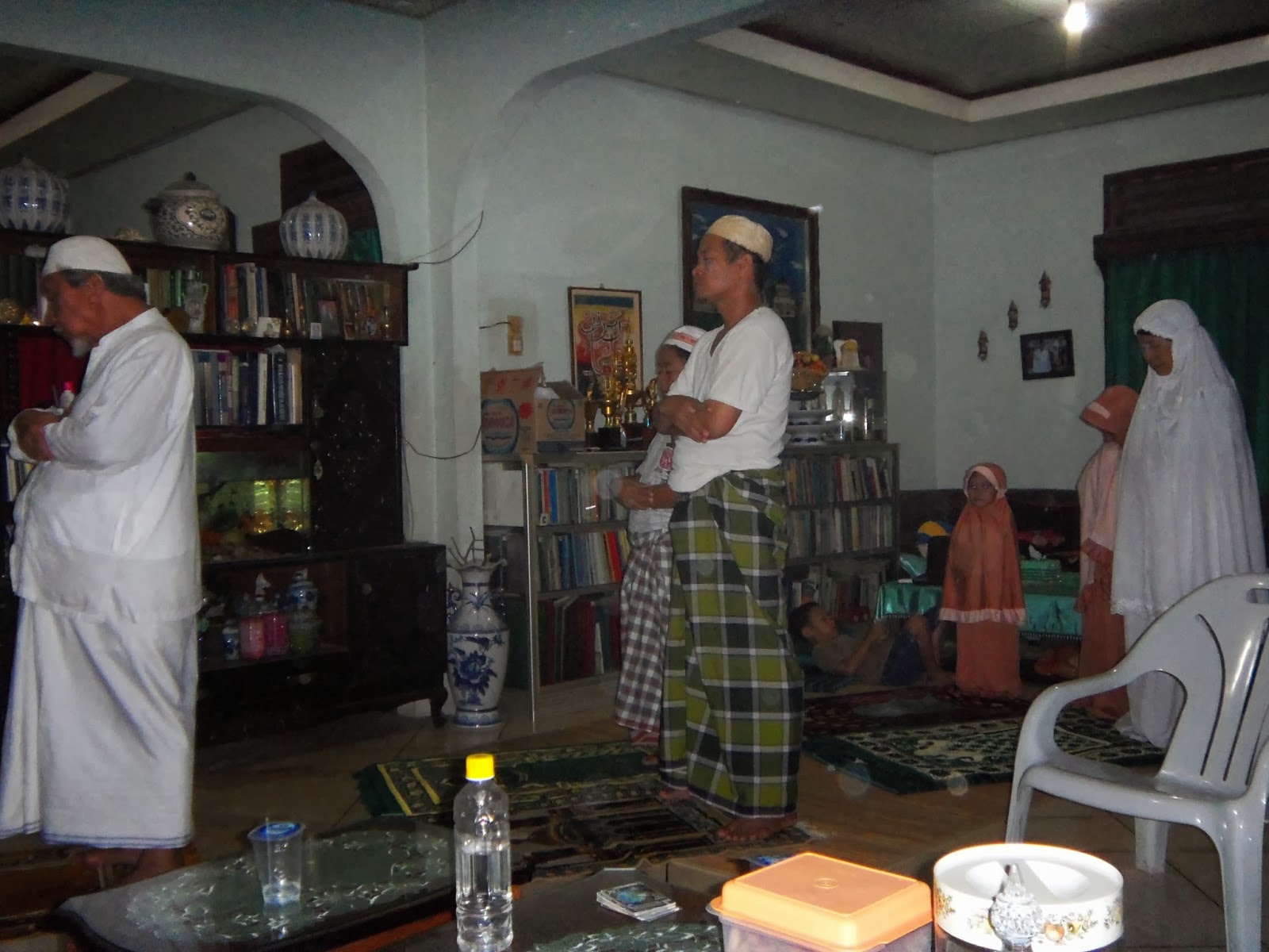 Keluarga bahagia sedang bersolat berjemaah di dalam rumah.